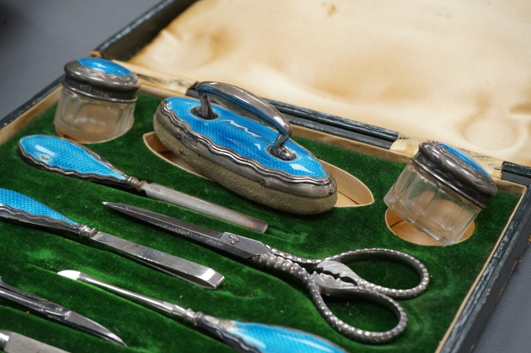A cased George V eight piece (ex 9 piece) manicure and toilet jar set, comprising seven silver and enamel mounted items, Boots Pure Drug Company, Chester and Birmingham, 1910, together with a matching pair of steel sciss